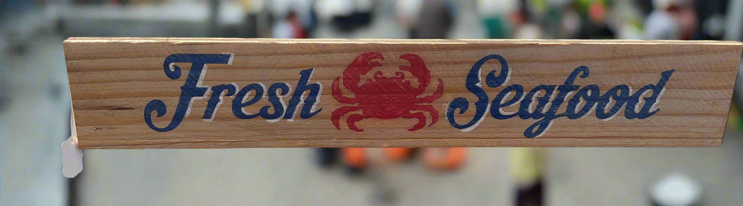 Wooden sign with 'Fresh Seafood' and a red crab illustration on a blurred background